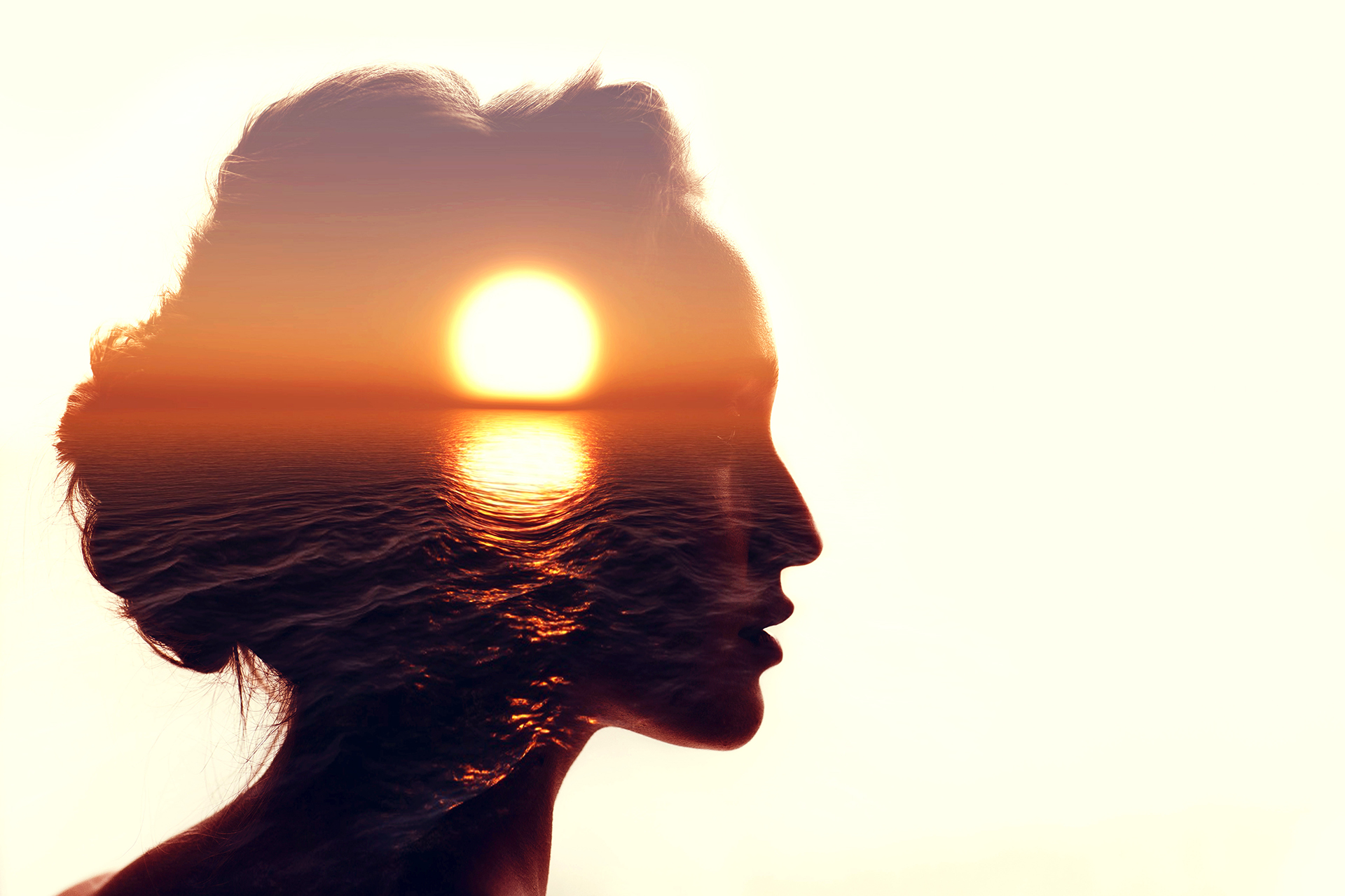 Double-exposure portrait of a woman in profile with an ocean sunset visible within her silhouette